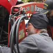 Two men examine the underside of a tractor.A closeup of gloved hands cleaning diesel fuel out of the canister that normally covers the fuel filter.