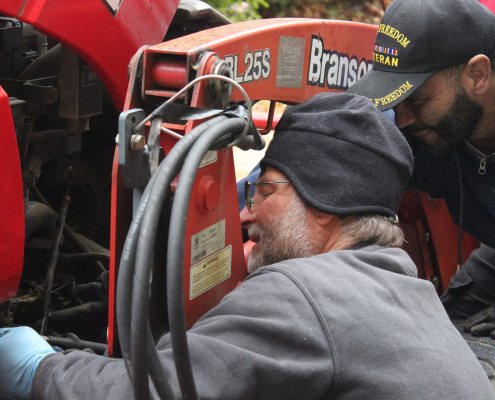 Two men examine the underside of a tractor.A closeup of gloved hands cleaning diesel fuel out of the canister that normally covers the fuel filter.