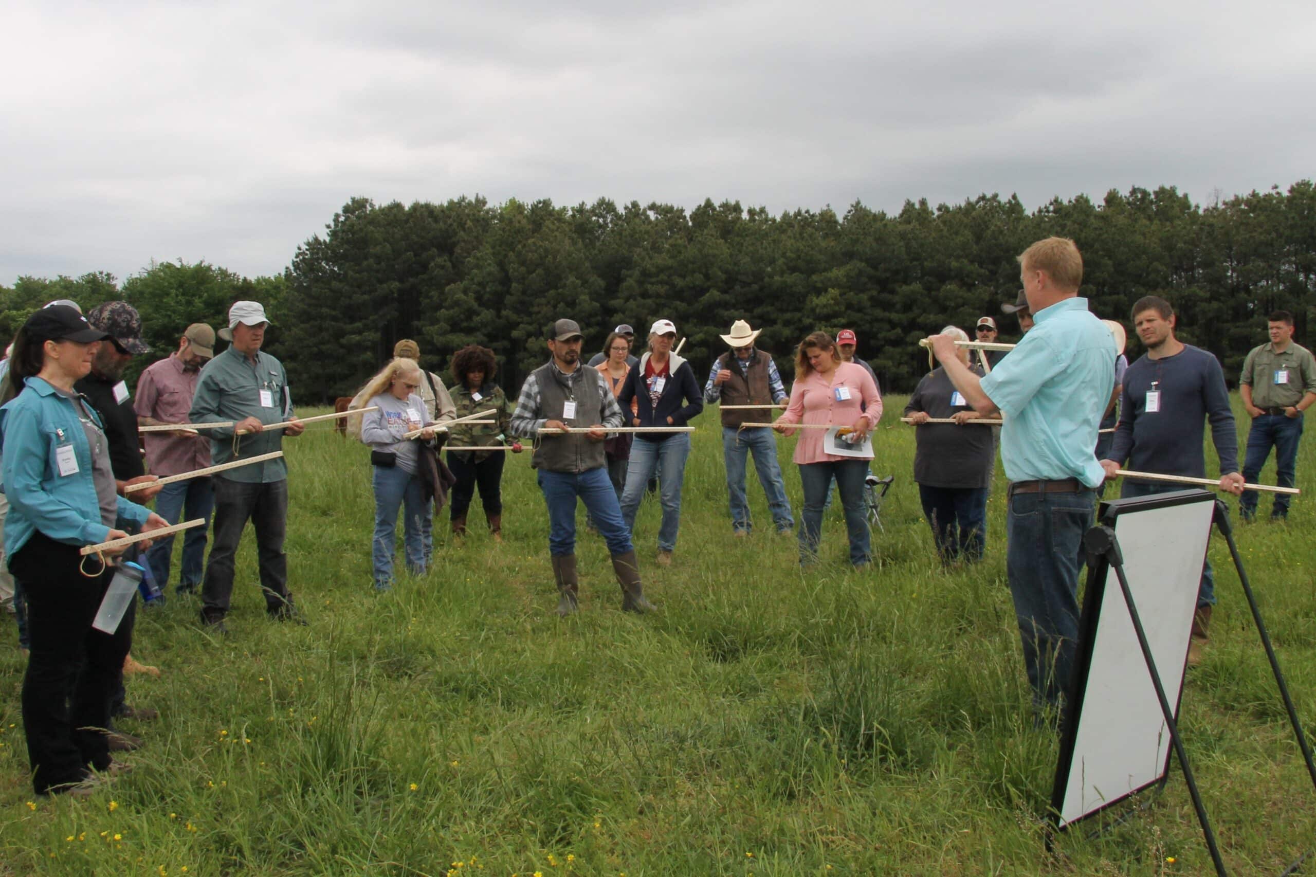 Man in a field instructing people with yard sticks.