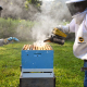 Two people in bee suits on either side of an open Langstroth beehive, one of them adding smoke to the hive.