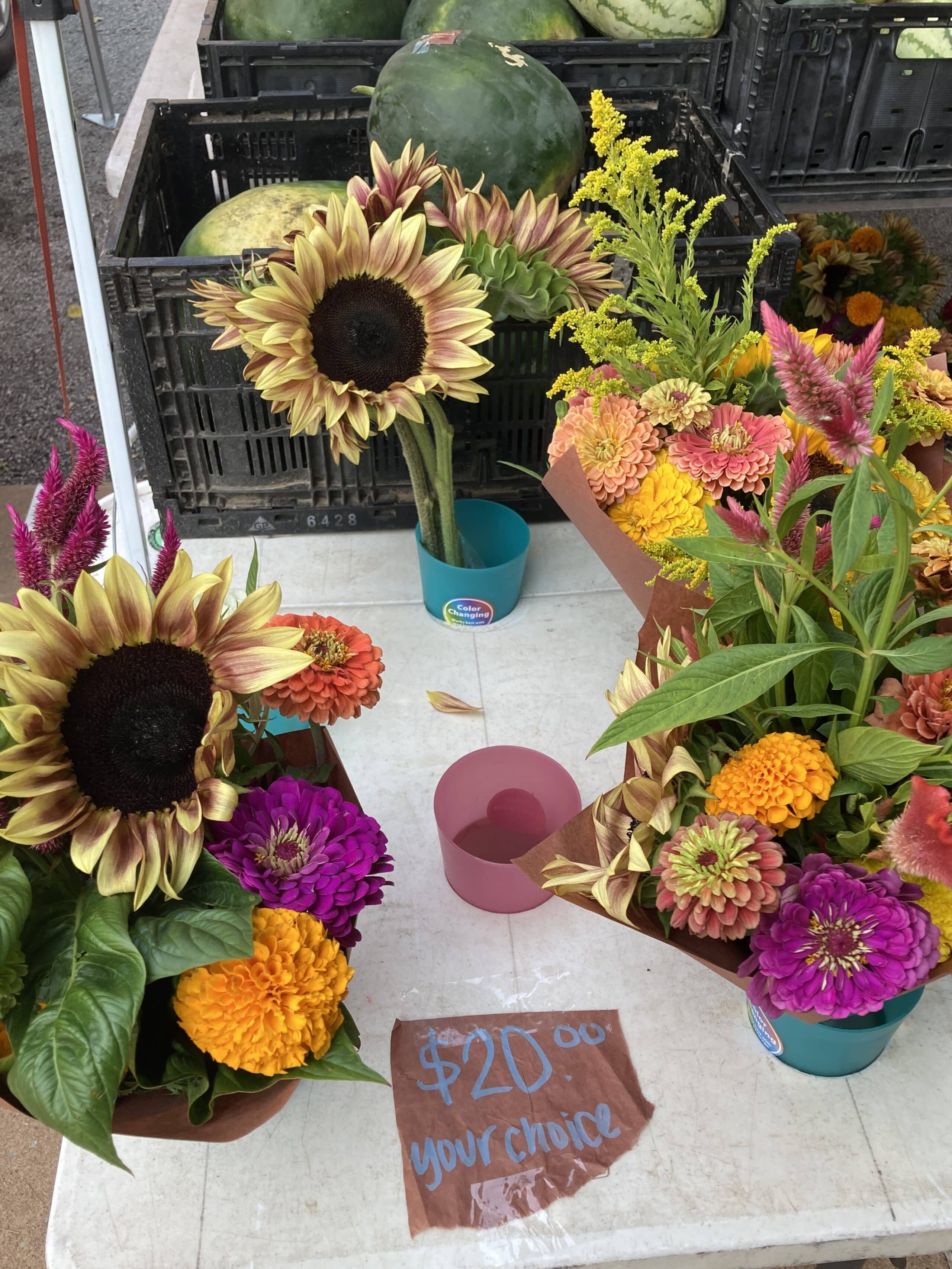 Mixed bouquets of sunflowers, zinnias, and other blooms on display at a Farmers Market table.