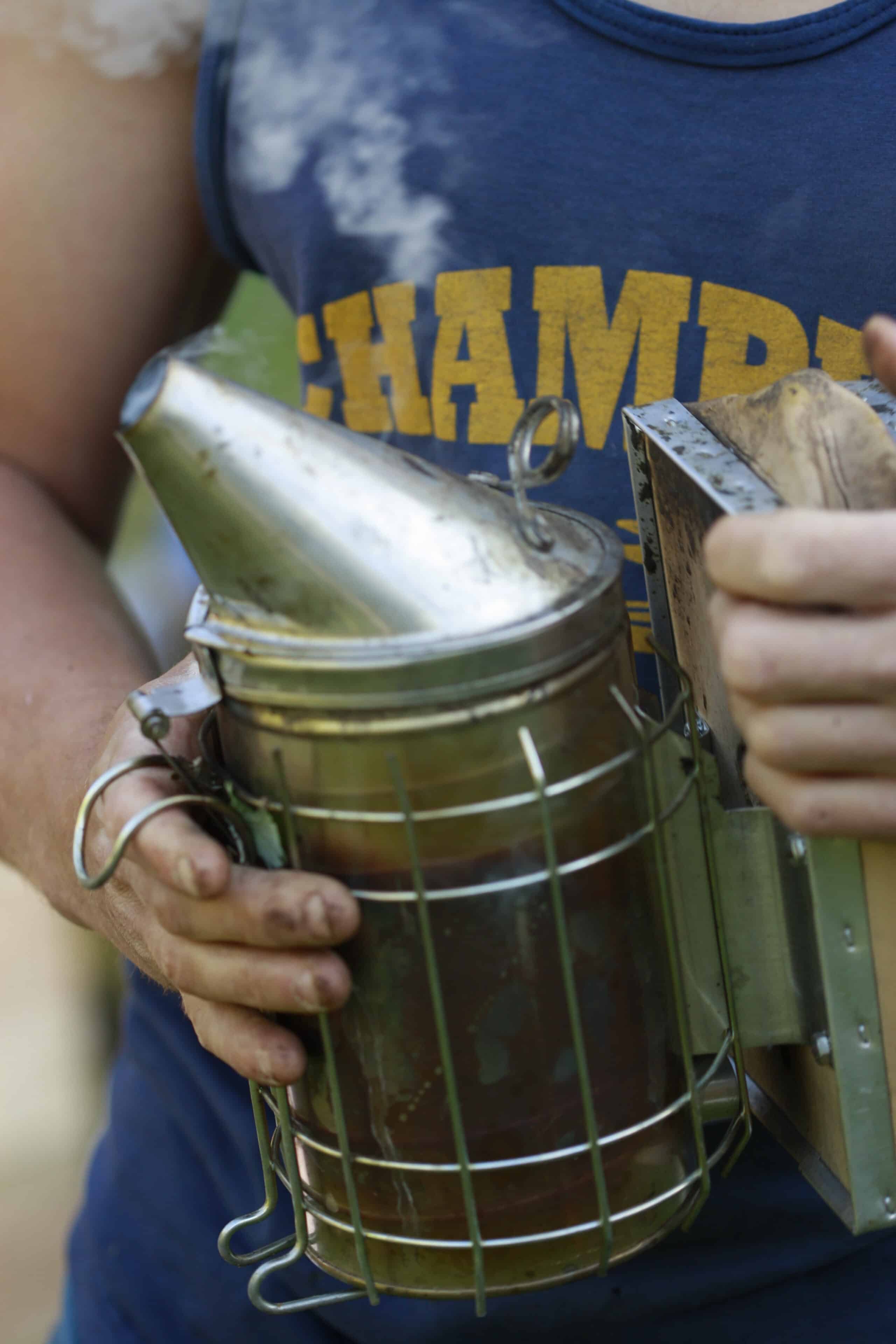 Close-up photo of a person holding a metal smoker used in beekeeping. 