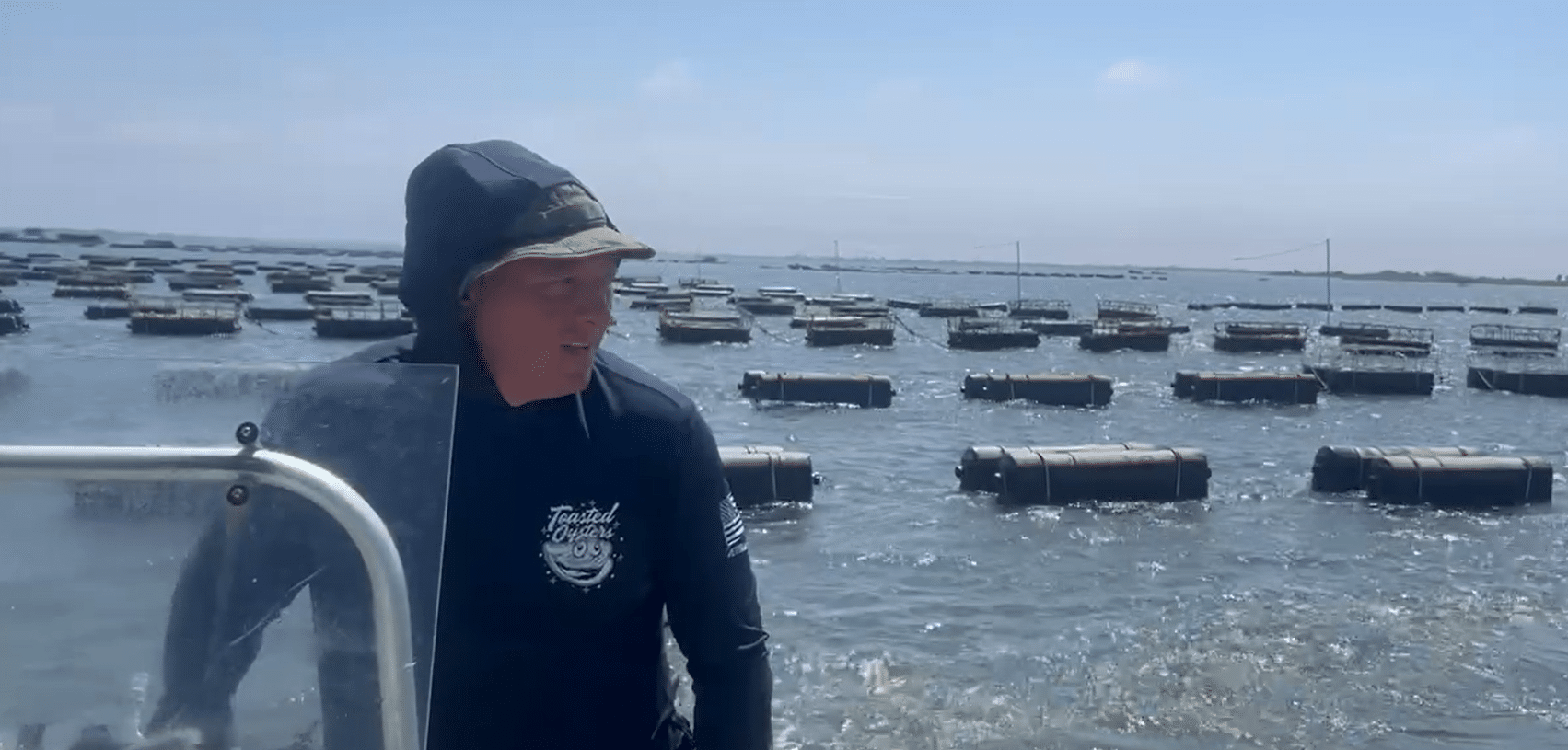 A man in a hooded jacket steers the boat away from the floating cages of the oyster farm. 