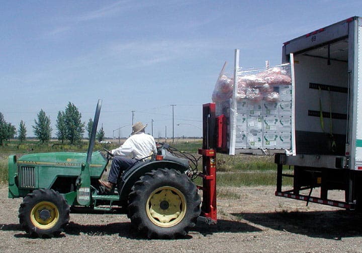man with a tractor loading a crate with boxes into a truck