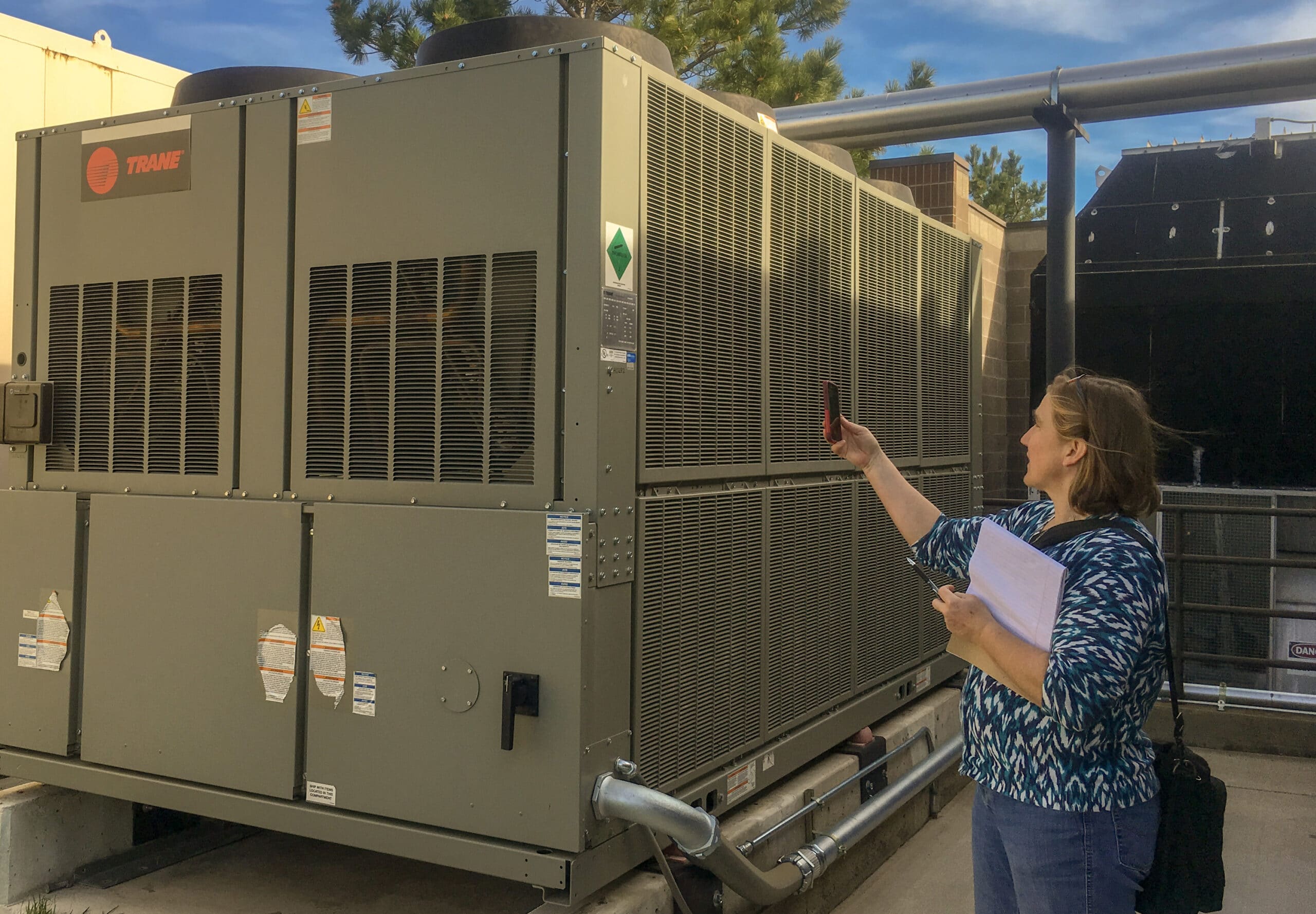 Una mujer está de pie junto a una gran unidad de climatización mientras realiza una auditoría energética.