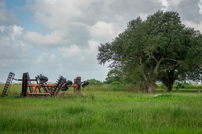 field equipment parked in grass near a tree under sky with clouds