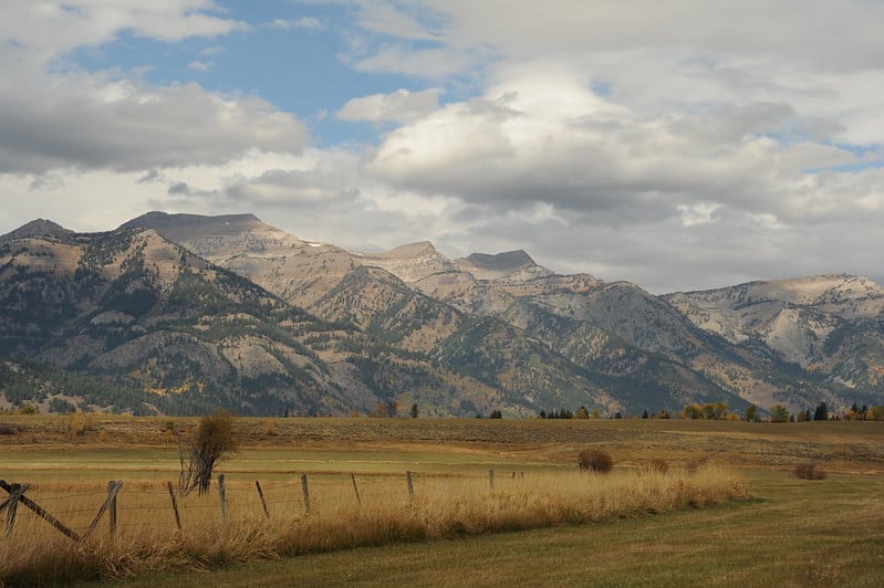 hayfield, rangeland, and distant mountains under blue sky with clouds