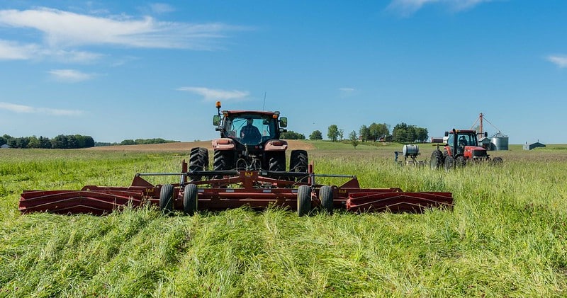 tractor pulls a roller crimper away across a field of cover crop under blue sky