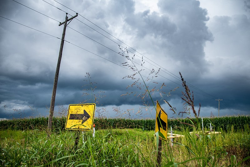 storm clouds above farm ground, power lines, and arrow road signs