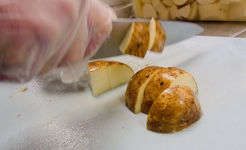 a hand holding a knife chops potatoes on a cutting board