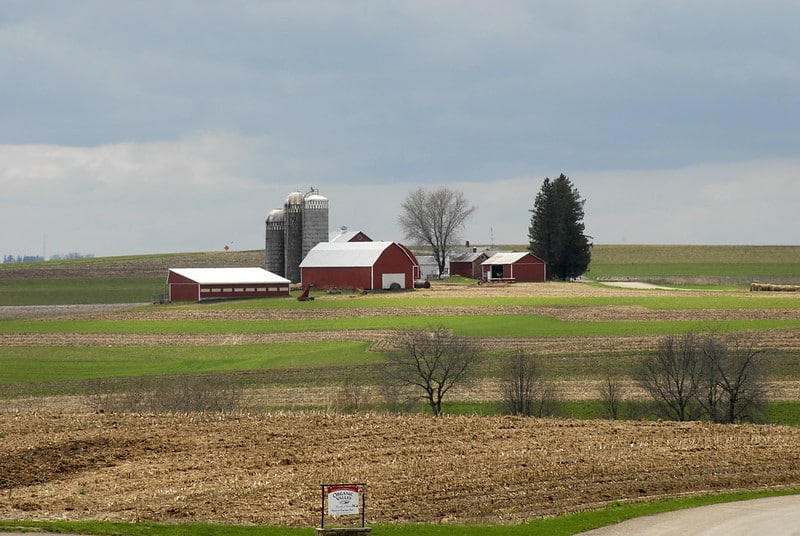 farm landscape with fields, barn, buildings, silos, and trees
