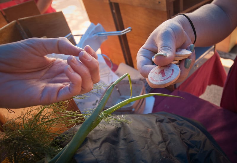 two hands exchange a wooden token above vegetables
