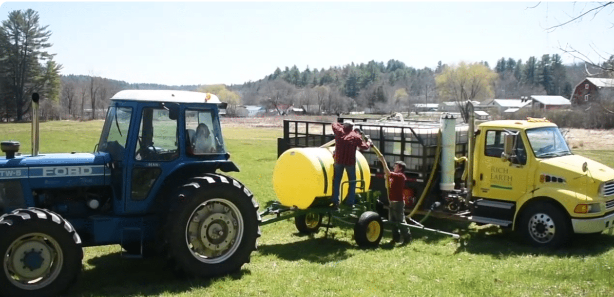 A tractor pulling a spray tank being filled by a tank truck.