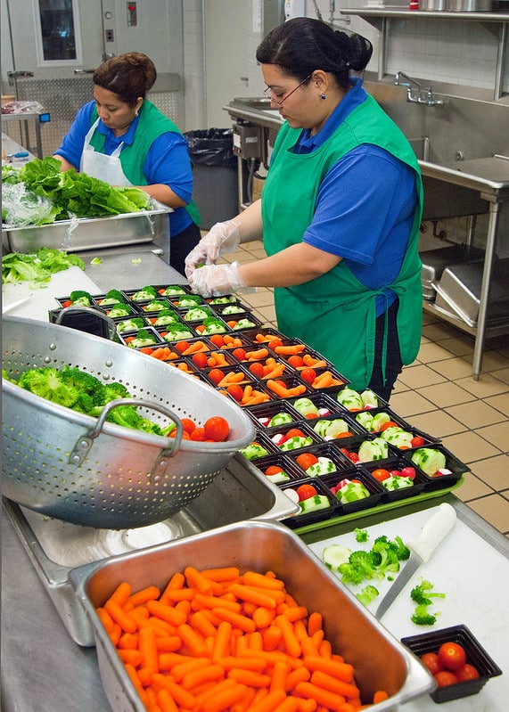 school food service workers assemble vegetable salads on trays
