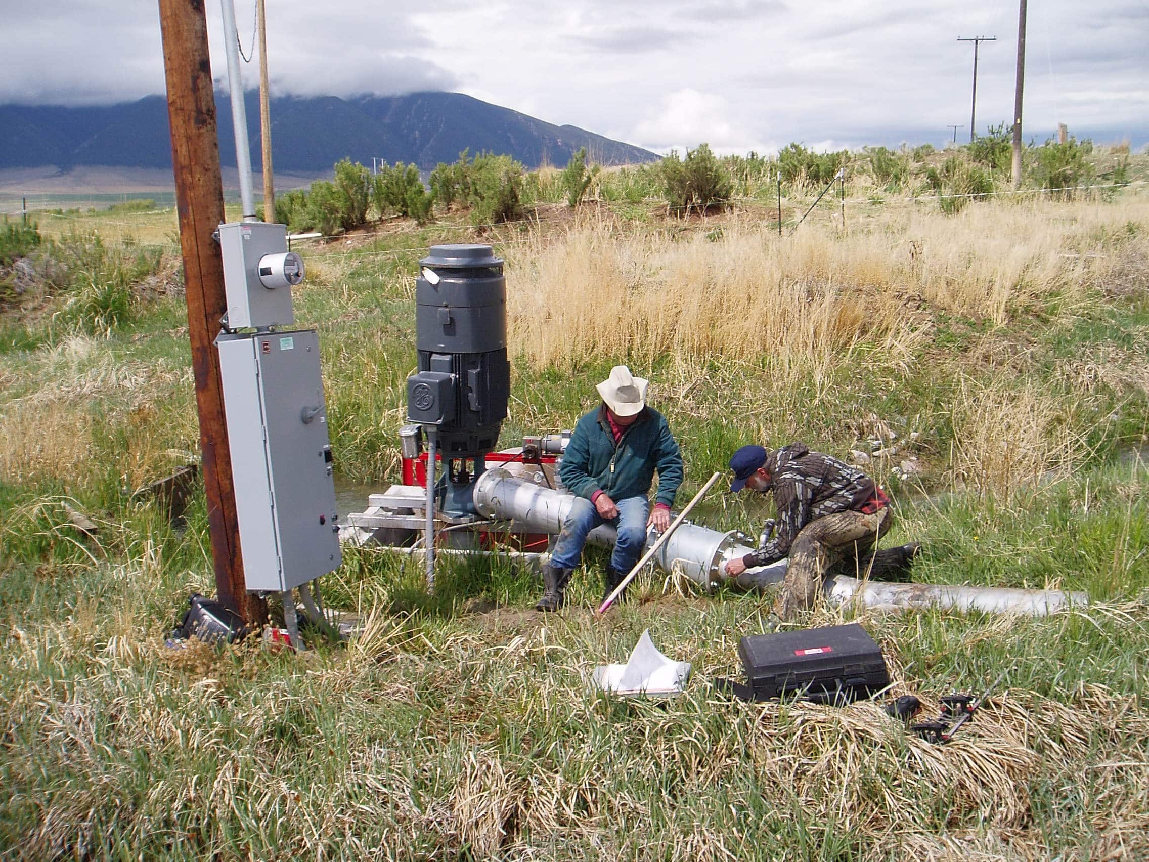 Two people working with irrigation equipment in a rangeland landscape
