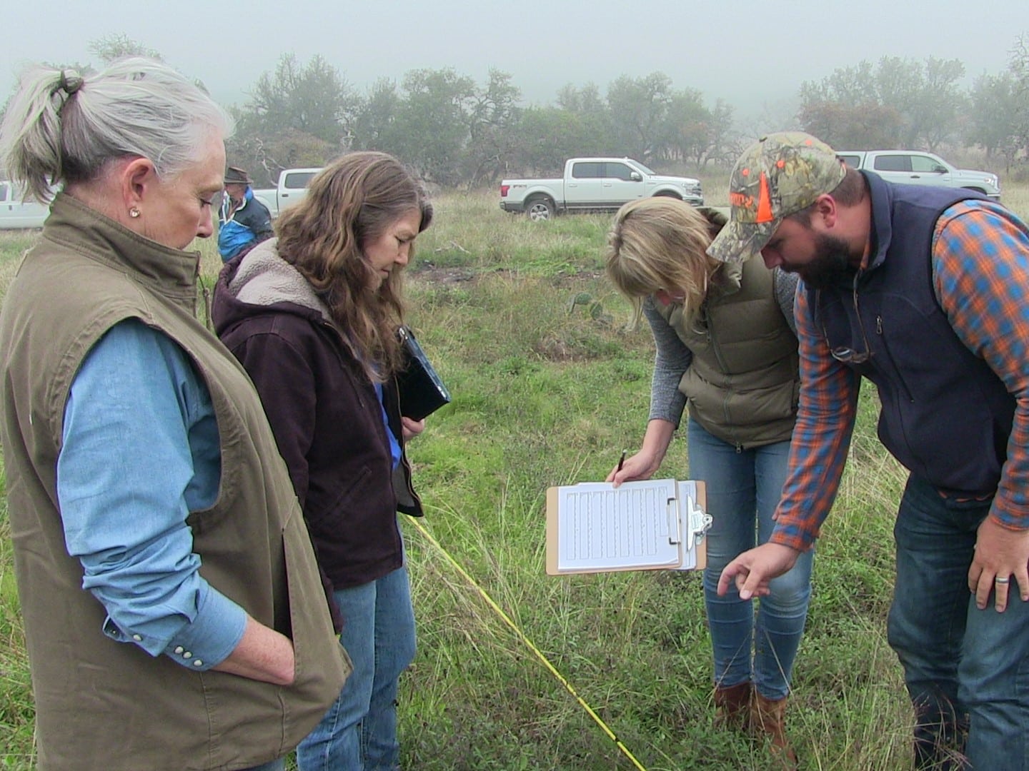 four people, one holding a clipboard, look down at pasture forage