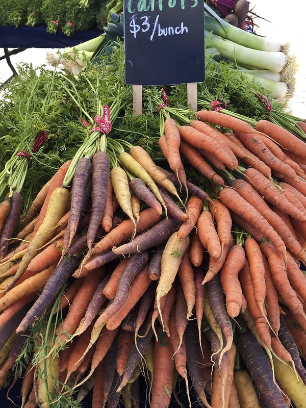 racimos de zanahorias de colores con hojas, en exhibición en el mercado de agricultores