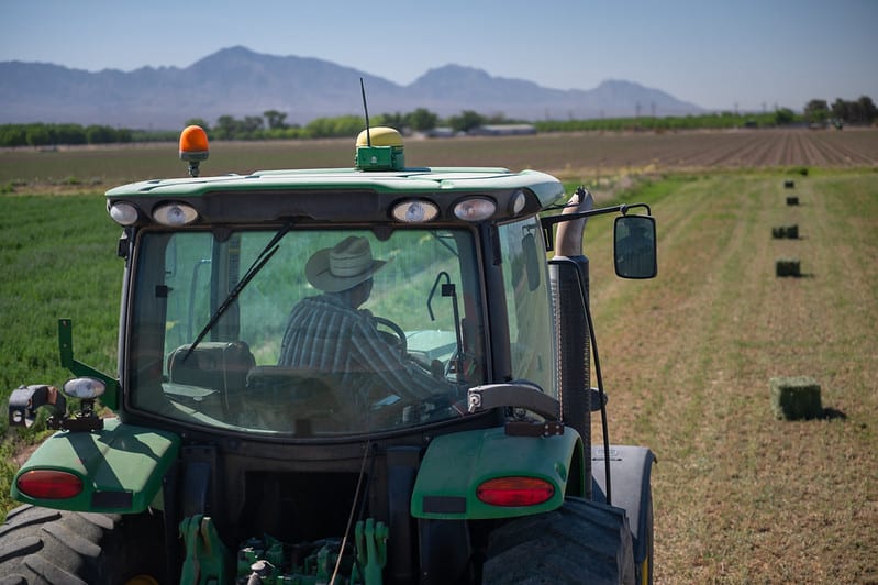 tractor moving away through hay field with mountains in background